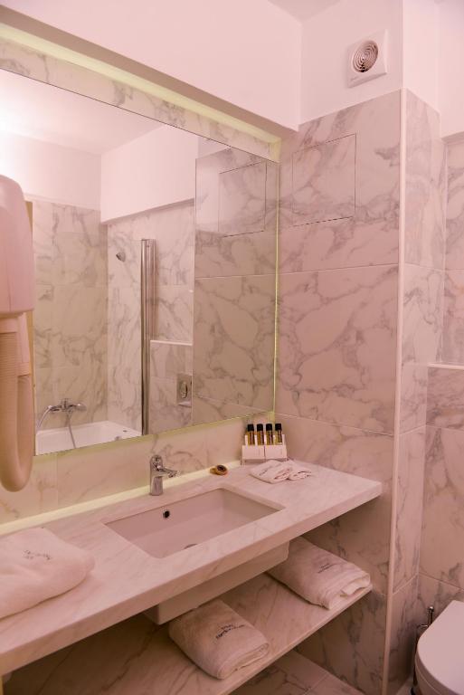 Mūsdienīgs vannas istabas interjers ar marmora apdari, izsmalcinātu izskatu un atbilstošām higiēnas precēm. Apgaismojums pie spoguļa rada siltu atmosfēru.