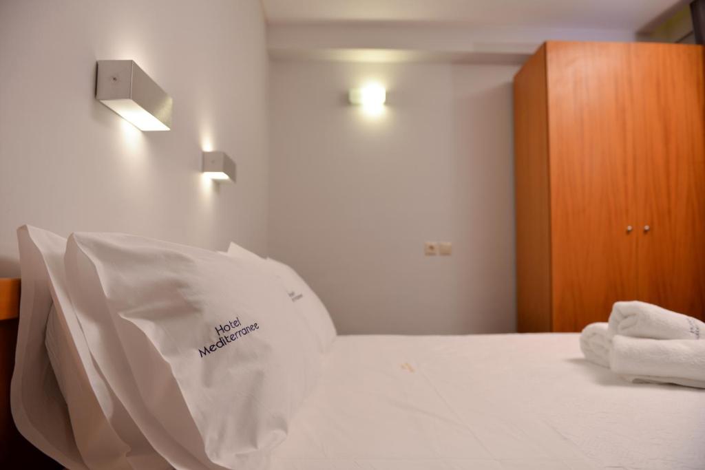 Mūsdienīga viesnīcas numura interjers ar gultu, spilveniem un dvieļiem. Sienas apgaismojums un koka skapis piešķir telpai siltumu un komfortu.