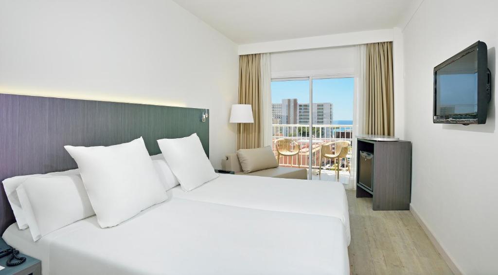 Mūsdienīga viesnīcas numura interjers ar divām gultām, televizoru un balkonu, no kura paveras skats uz jūru. Gaismas toņi un minimālisma stils rada patīkamu atmosfēru.