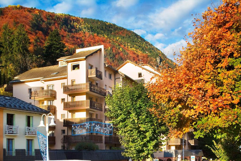 Rudens ainava ar mājām un krāsainām lapām, kas rotā apkārtni kalnu pakājē. Mājās ir balkoni un apkārt ir zaļumi, kas piešķir skatuves dzīvīgumu.