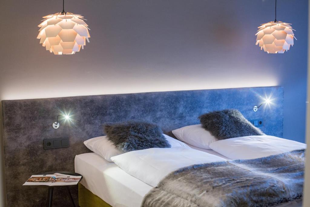 Moderns guļamistabas interjers ar divguļamo gultu, dekoratīvu apgaismojumu un mīkstiem spilveniem. Stilīgas lampas pie griestiem piešķir telpai siltu atmosfēru.