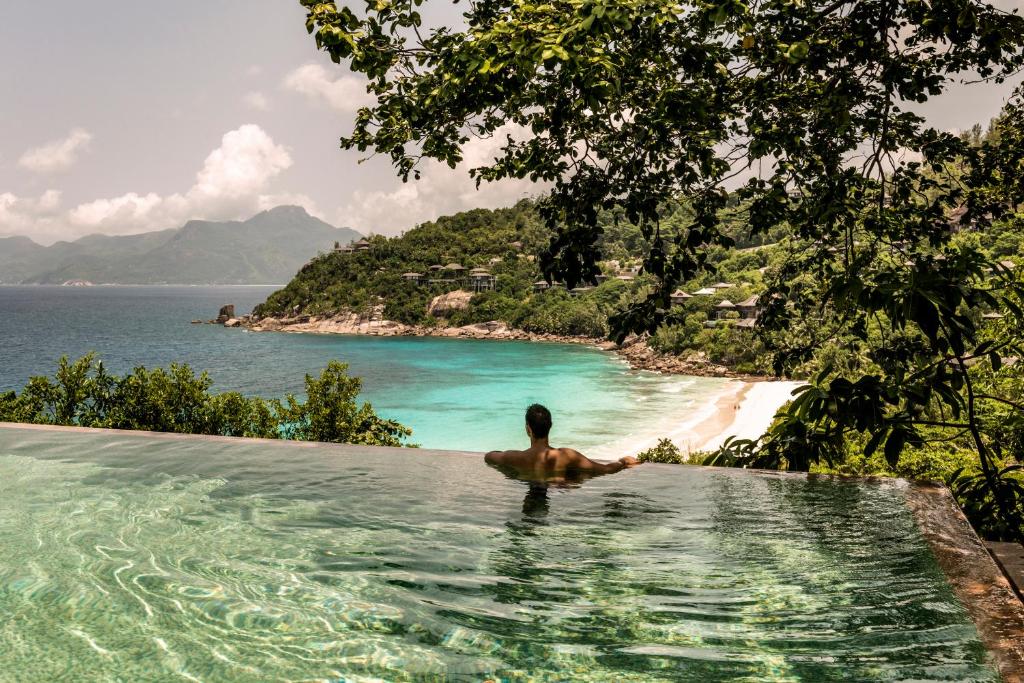 Four Seasons Resort Seychelles bezgalības baseins ar skatu uz tirkīzzilo okeāna līci un zaļajiem pakalniem.