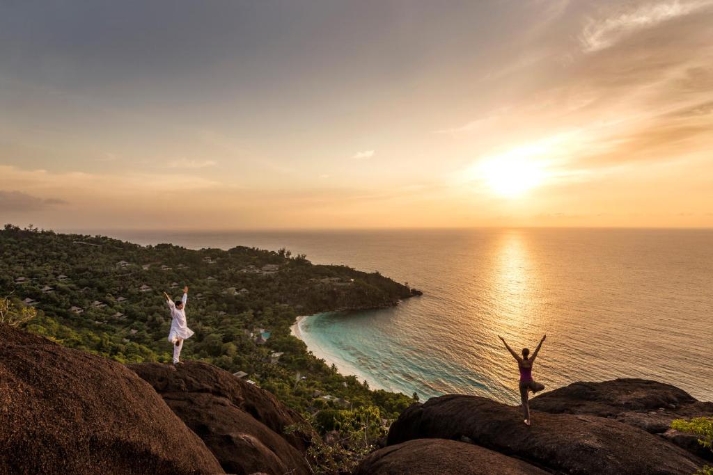 Joga uz granīta klintīm saulrietā Four Seasons Resort Seychelles ar skatu uz okeāna līci