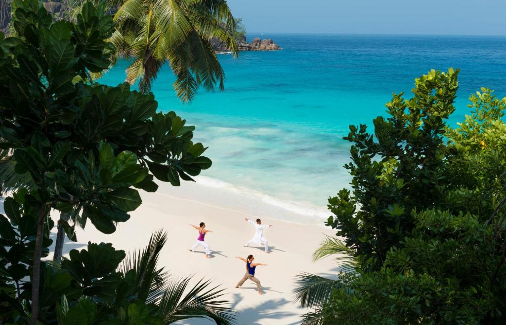 Joga baltu smilšu pludmalē Four Seasons Resort Seychelles piekrastē ar tirkīzzilu ūdeni fonā