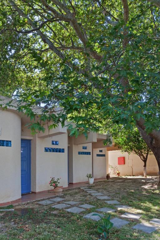 Mājas fasāde ar zilu durvju un logu akcentiem, ko ieskauj zaļš koks un zāliena ceļš. Ideāla ainava mierīgai atmosfērai.