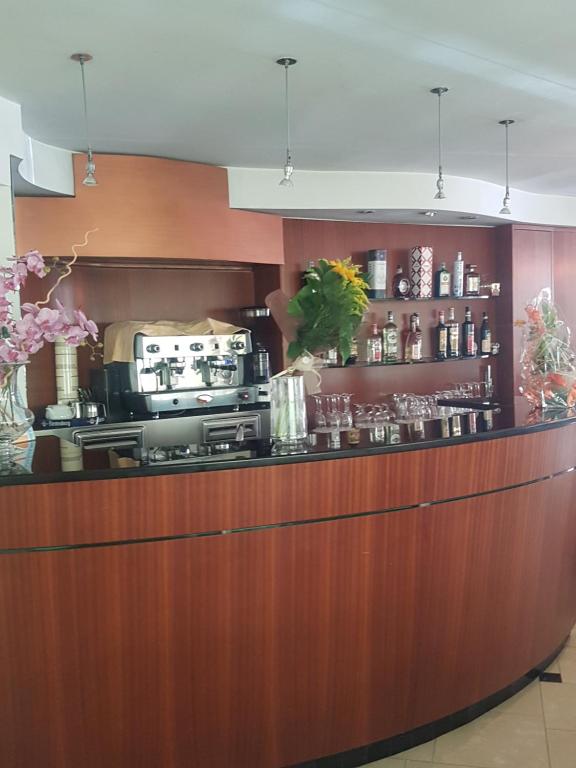 Mūsdienīgs bārs ar koka apdari, kas ietver kafijas aparātu un dažādu dzērienu plauktus. Dekorēts ar ziediem un glāzēm.