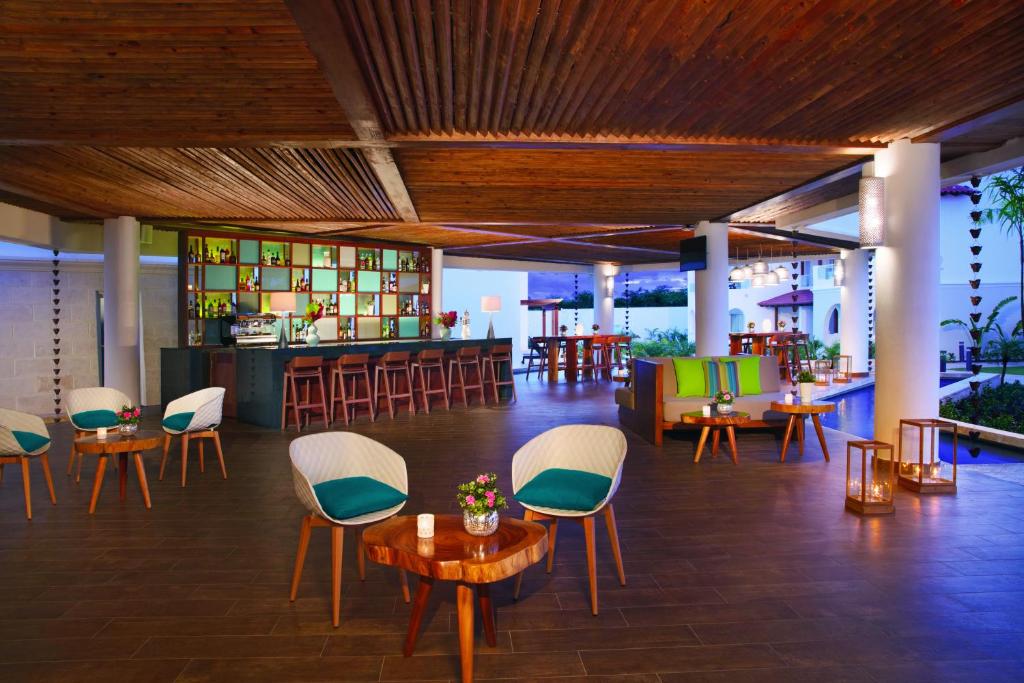 Mūsdienīgs bārs ar koka griestiem un stilīgām mēbelēm, kurā ir ērti sēdvietas un dzērienu plaukti. Telpa ir izgaismota ar mīksto apgaismojumu, radot relaksējošu atmosfēru.