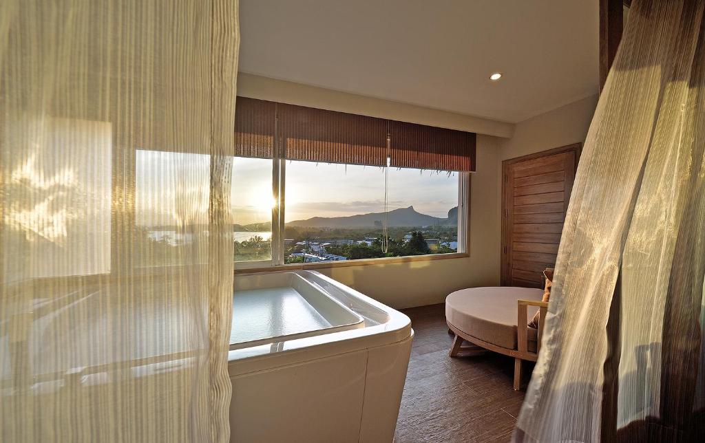 Mūsdienīgs interjers ar vannu un logu, no kura paveras skats uz kalnu ainavu un saulrietu. Gaismas plūsma caur aizkariem rada mierīgu atmosfēru.