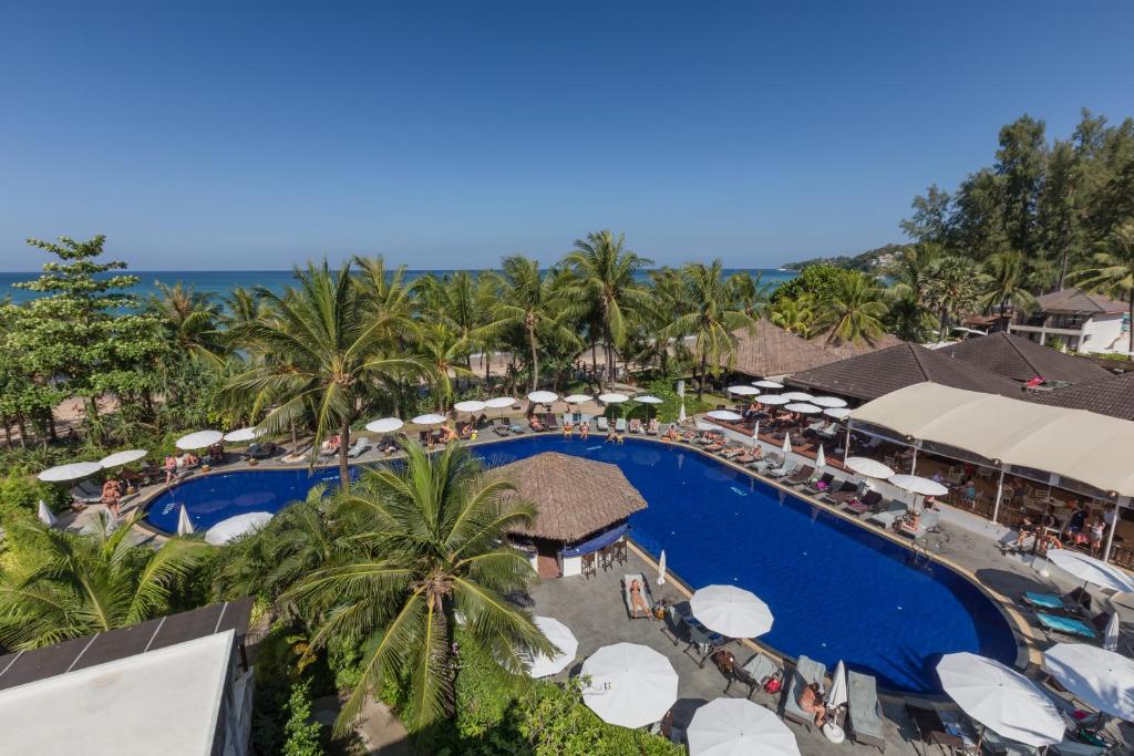 Viesnīcas baseins ar palmām un sauļošanās krēsliem, kas izvietoti ap to, skats uz jūru un saulainu debesi. Ideāla vieta atpūtai un relaksācijai.