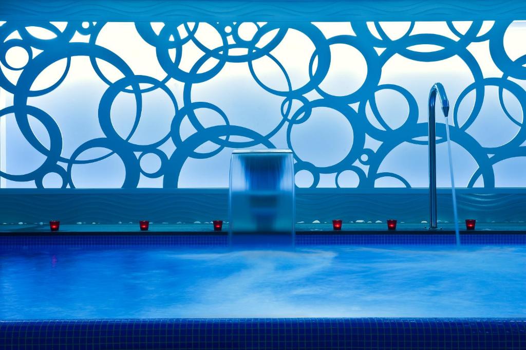 Mūsdienīgs spa ar zilu ūdeni un dekoratīvu sienu ar aplīšu dizainu, radot relaksējošu atmosfēru.