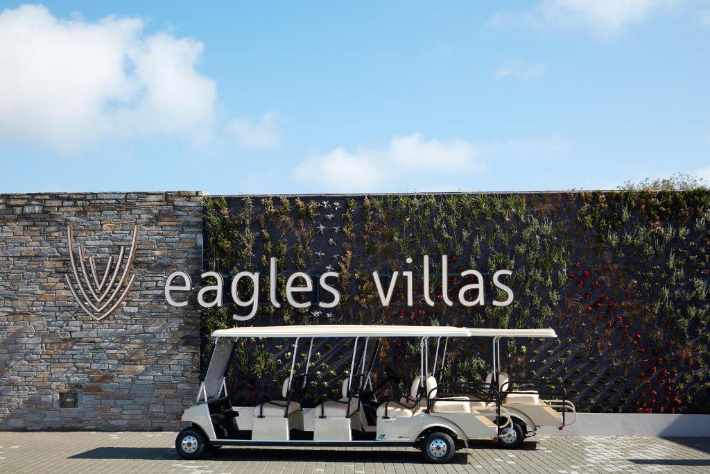 Eagles Villas logo pie akmens sienas ar zaļumiem un golfa transportlīdzeklis priekšplānā.