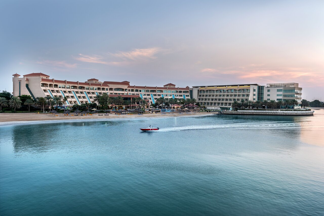 Luksusa viesnīca pie pludmales ar apkārtējiem palmām un kuģīti, kas pārvietojas pa mierīgu ūdeni. Ideāla vieta atpūtai un izklaidei. panoramic view with beach and pools