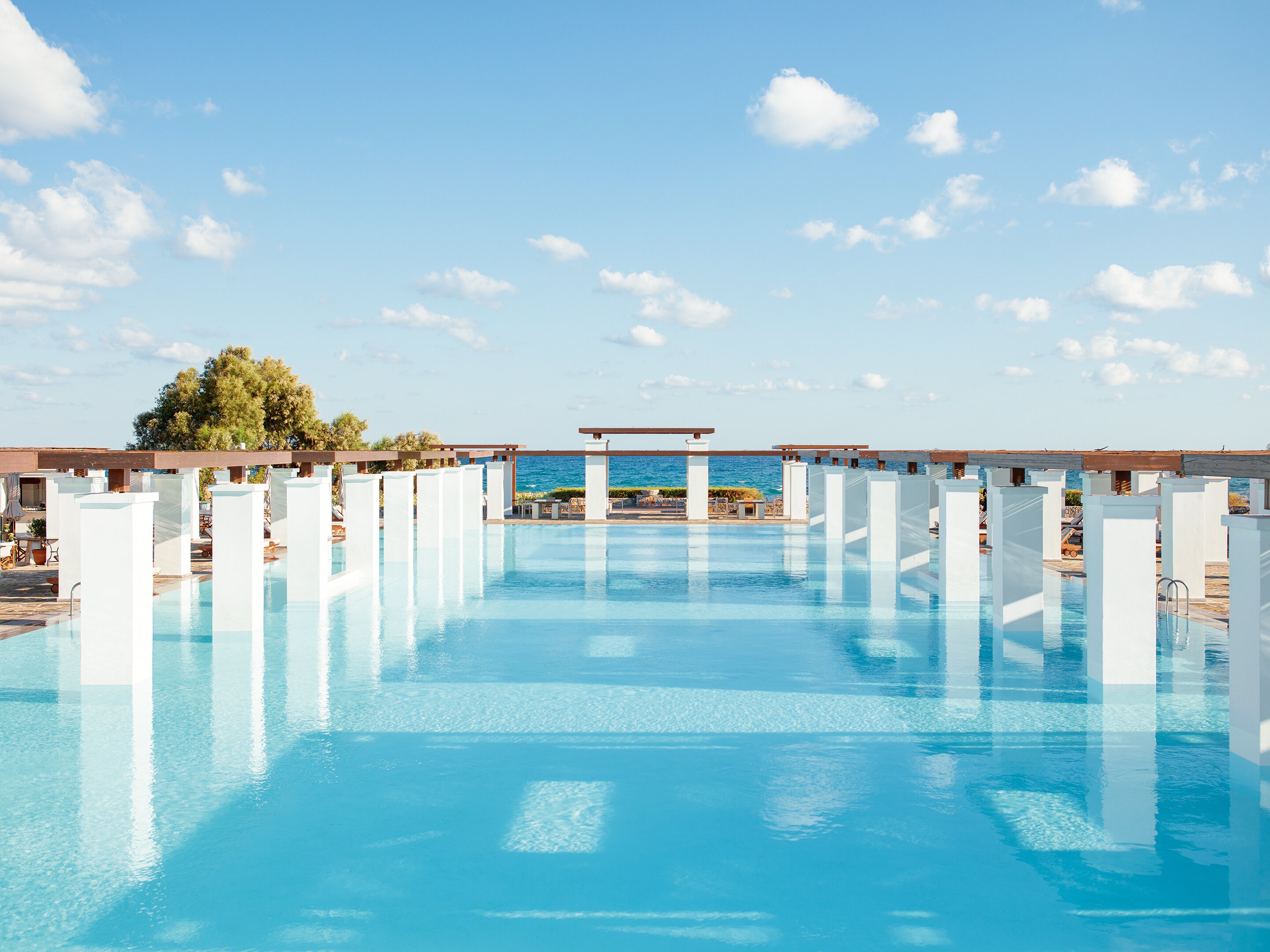 Vasaras atpūtas vieta ar plašu baseinu, kurā atspoguļojas debesis un apkārtējā ainava. Mierīga atmosfēra un moderns dizains, kas aicina uz relaksāciju. panoramic view with beach and pools
