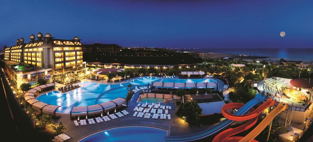 Peldbaseins un viesnīcas komplekss pie jūras, izgaismots naktī ar skatu uz debesīm un mēnesi. Ideāla vieta atpūtai un izklaidei. panoramic view with beach and pools