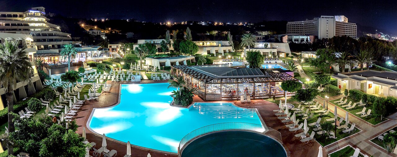 Lielisks nakts skats uz luksusa viesnīcu ar apgaismotu baseinu, palmām un atpūtas zonām. Viesnīcas arhitektūra un ainava veido relaksējošu atmosfēru. panoramic view with beach and pools
