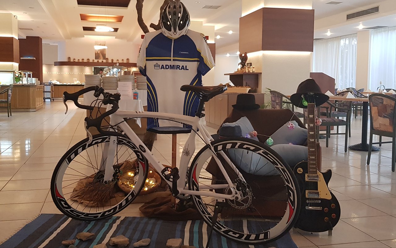 Olympos Beach Hotel interjers ar izstādītu šosejas velosipēdu, Admiral riteņbraukšanas kreklu un melnu elektrisko ģitāru.