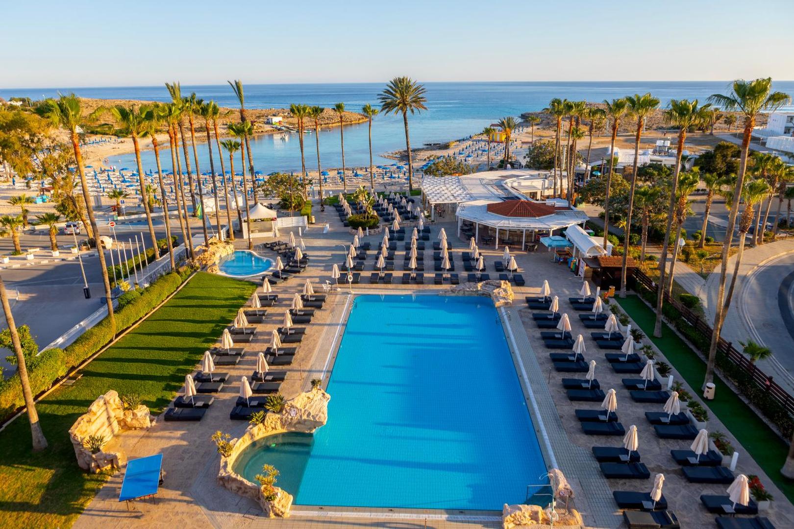 Pavlo Napa Beach Hotel plašā teritorija ar lielu āra baseinu, palmām un tiešu piekļuvi pludmalei Ajanapā, Kiprā