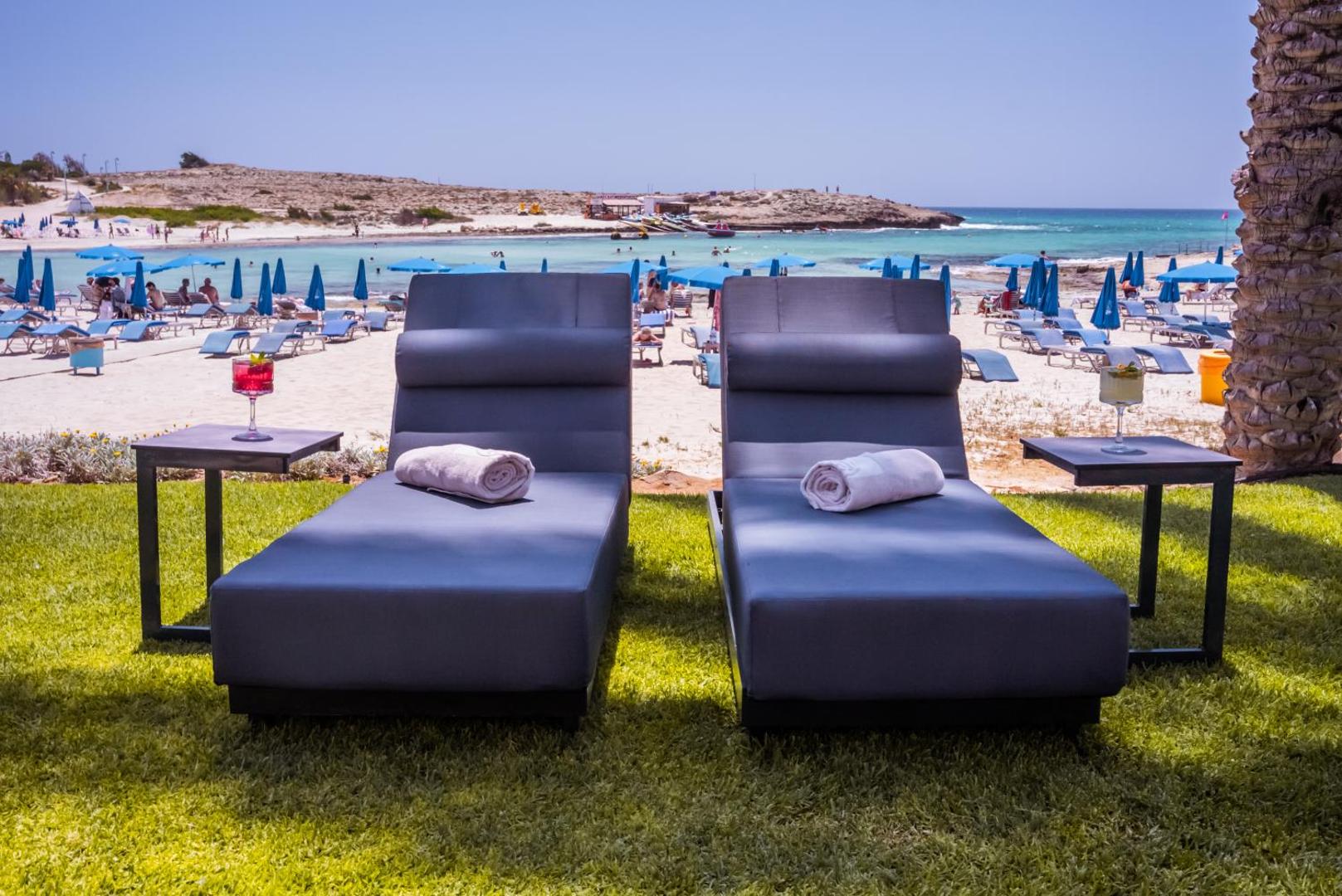 Pavlo Napa Beach Hotel atpūtas zona ar mīkstiem zviļņiem zālienā pie pludmales Aijanapā, Kiprā