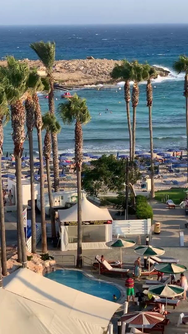 Skats no augšas uz Pavlo Napa Beach Hotel pludmali un niršanas centru Ajanapā — tirkīzzils ūdens, smilšu krasts un palmas