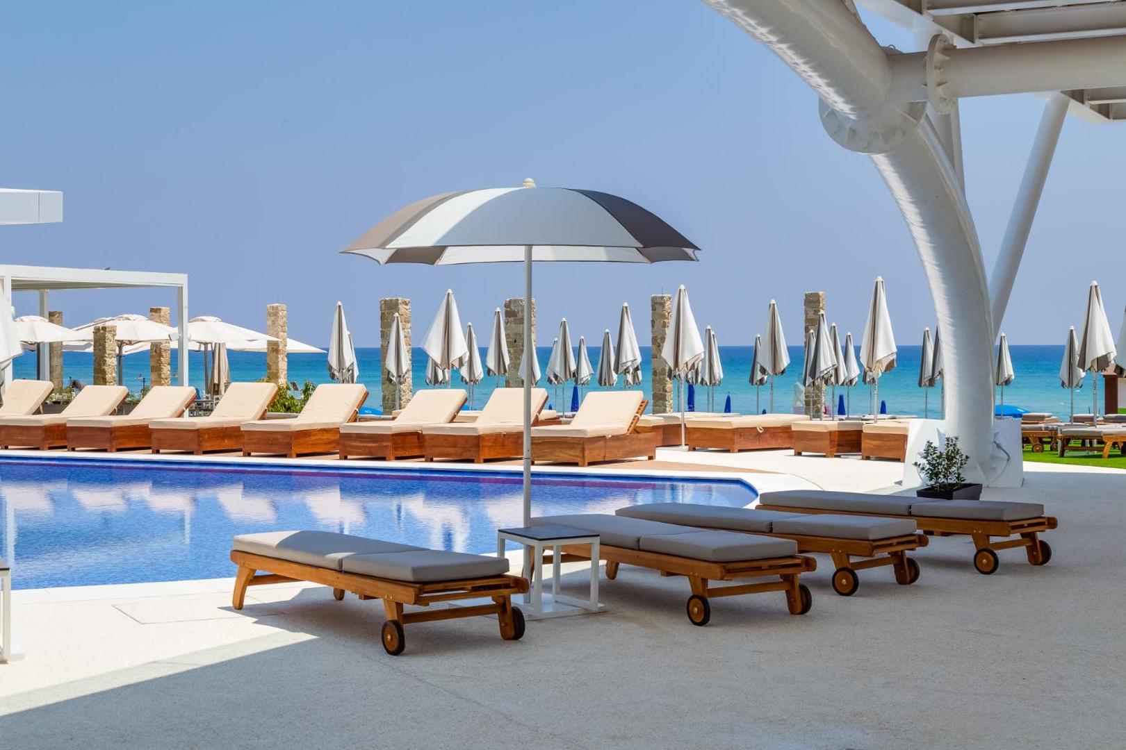 Flamingo Paradise Beach Hotel atpūtas zona ar ērtiem zviļņiem pie baseina — fonā redzama jūra un saulessargi Kipras piekrastē