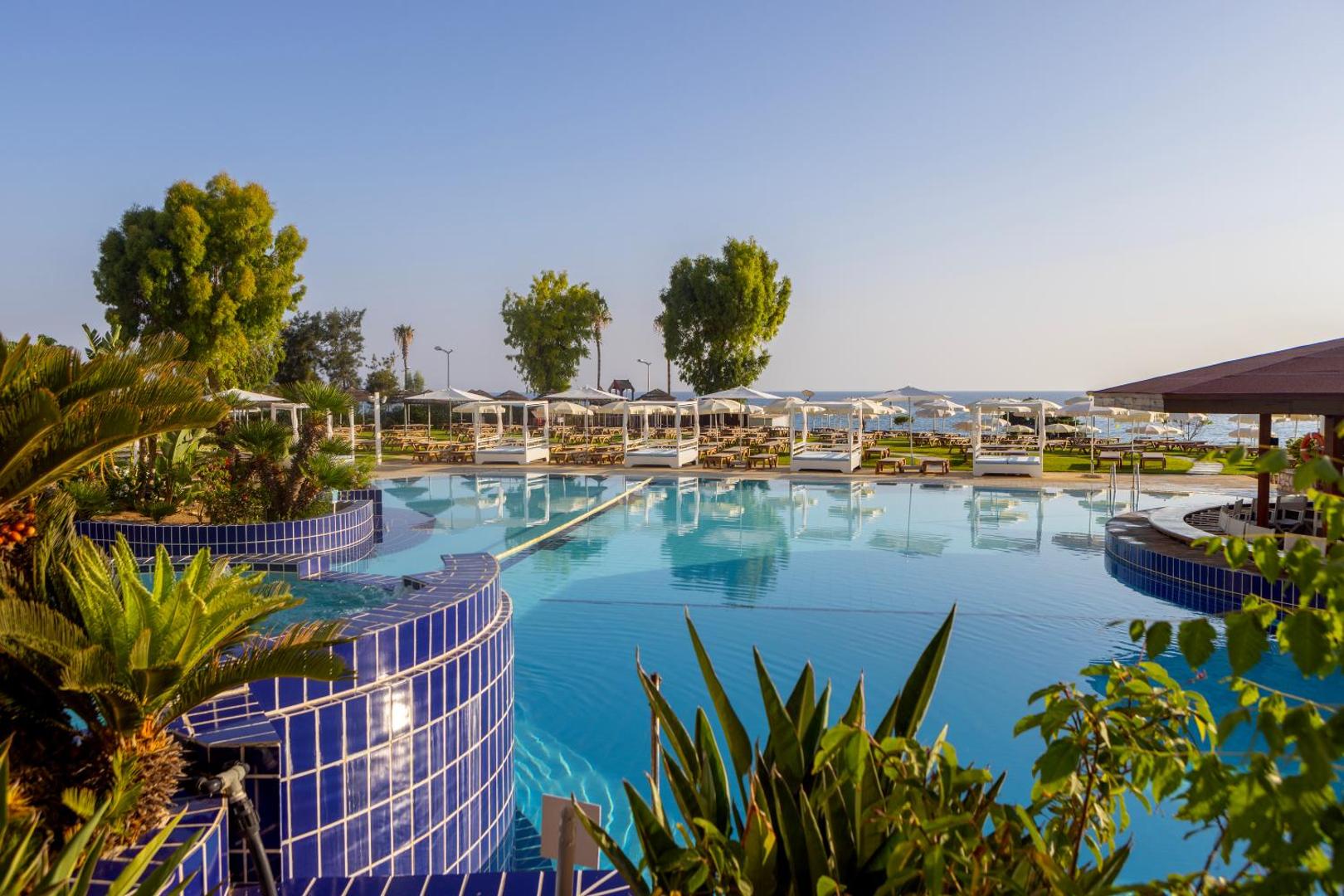 Viesnīcas Capo Bay Beach Hotel baseina zona ar hidromasāžas elementiem un bāru pie ūdens, apkārtnē palmas un zāliens