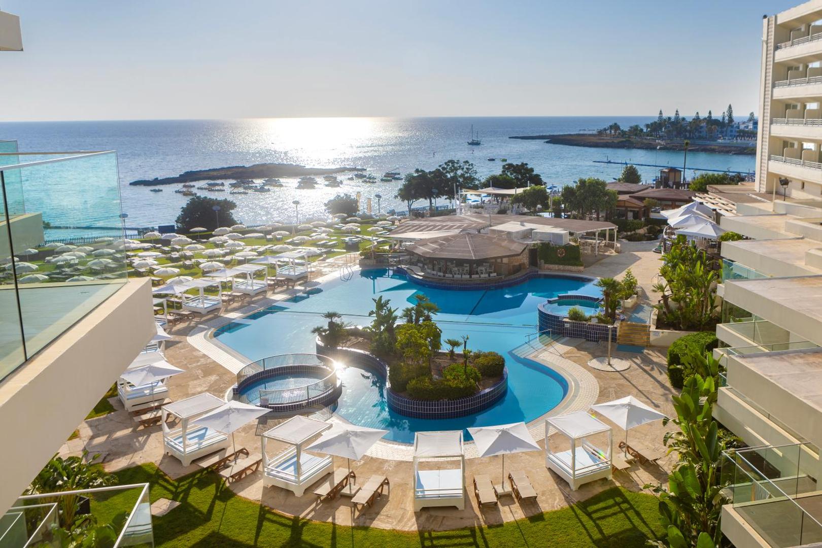 Capo Bay Beach Hotel plašā teritorija ar lagūnas tipa baseinu, saulessargiem un skatu uz jūru Protarasā, Kiprā
