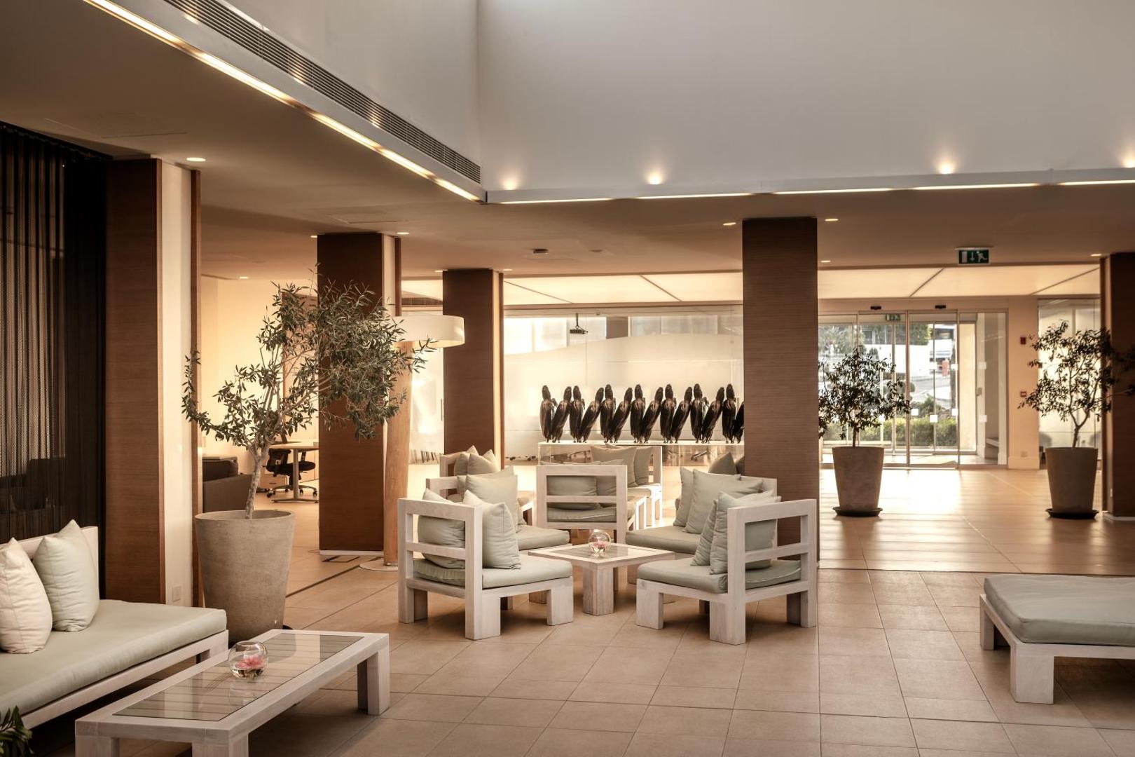 Capo Bay Beach Hotel lobby atpūtas zona ar mīkstiem krēsliem, olīvkokiem podos un modernu interjeru