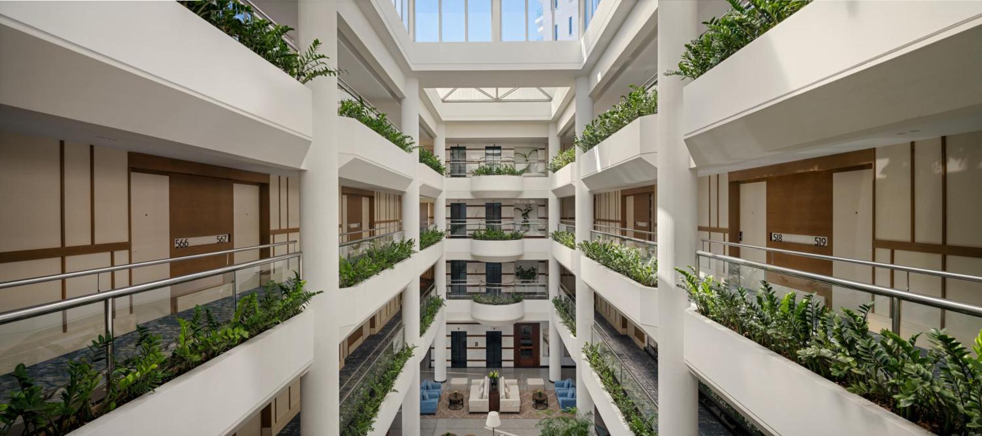 Mediterranean Beach Hotel modernais ātrija stila vestibils Limasolā ar vairākiem stāviem, telpaugiem uz balkoniem un stikla griestiem dabiskajam apgaismojumam