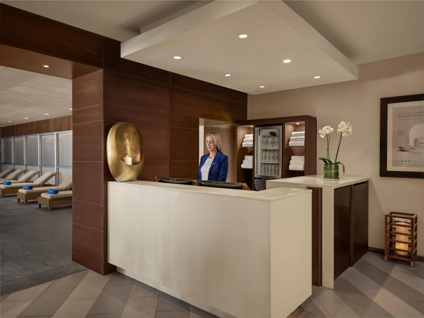 Mediterranean Beach Hotel spa centra recepcija ar darbinieci zilā uniformā, fonā redzami atpūtas krēsli un dvieļu plaukti