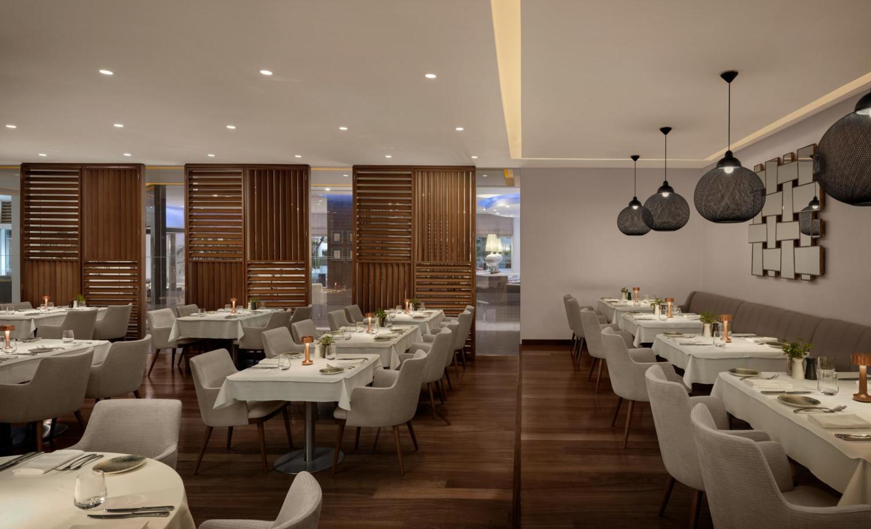 Mediterranean Beach Hotel iekštelpu restorāns ar baltiem galdautiem un modernām lampām — elegants dizains un mājīga atmosfēra