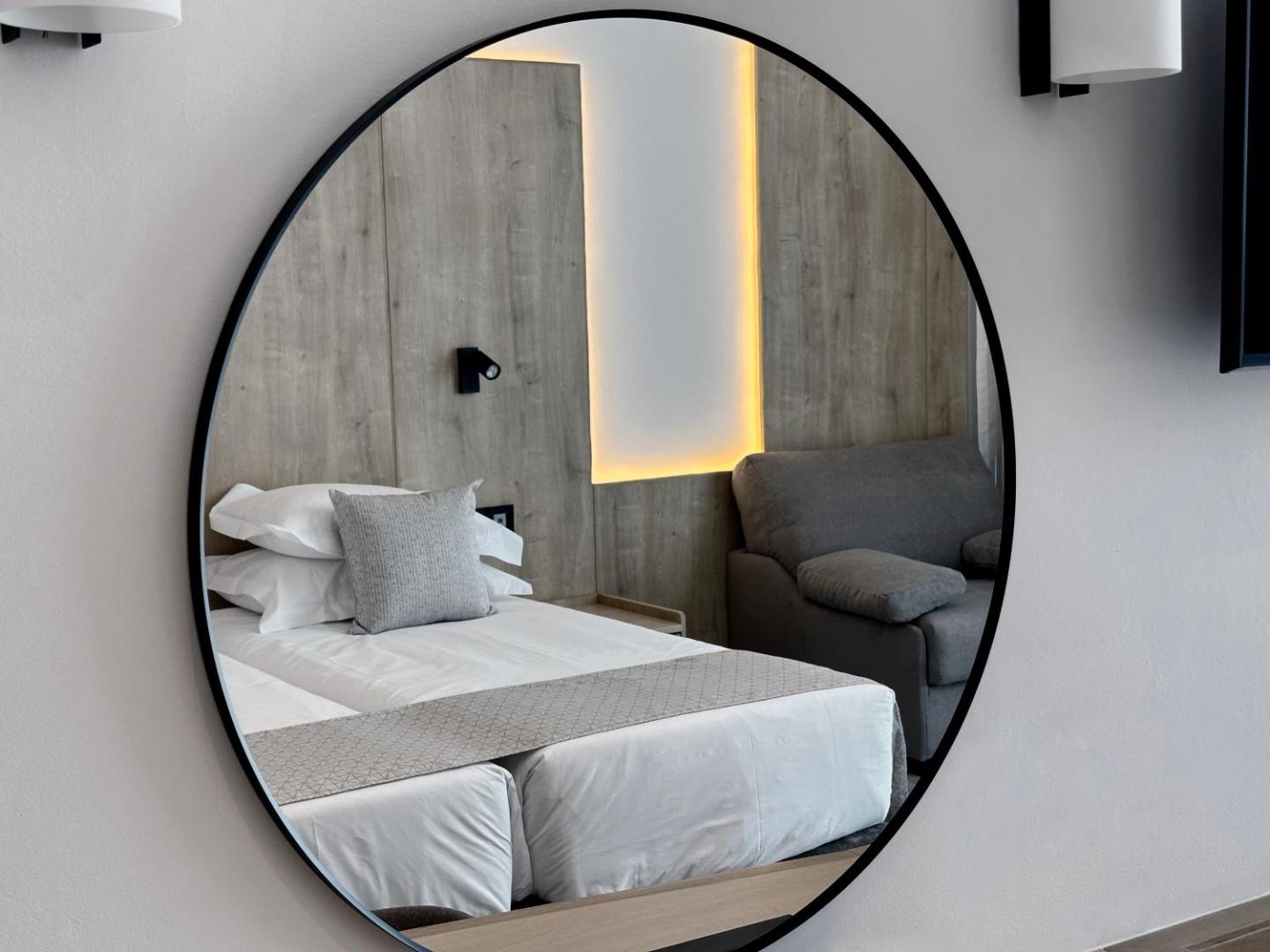 Sofianna Resort & Spa numura interjers ar apaļu spoguli, kurā atspoguļojas divguļamā gulta un pelēks atpūtas krēsls Pafas kūrortā