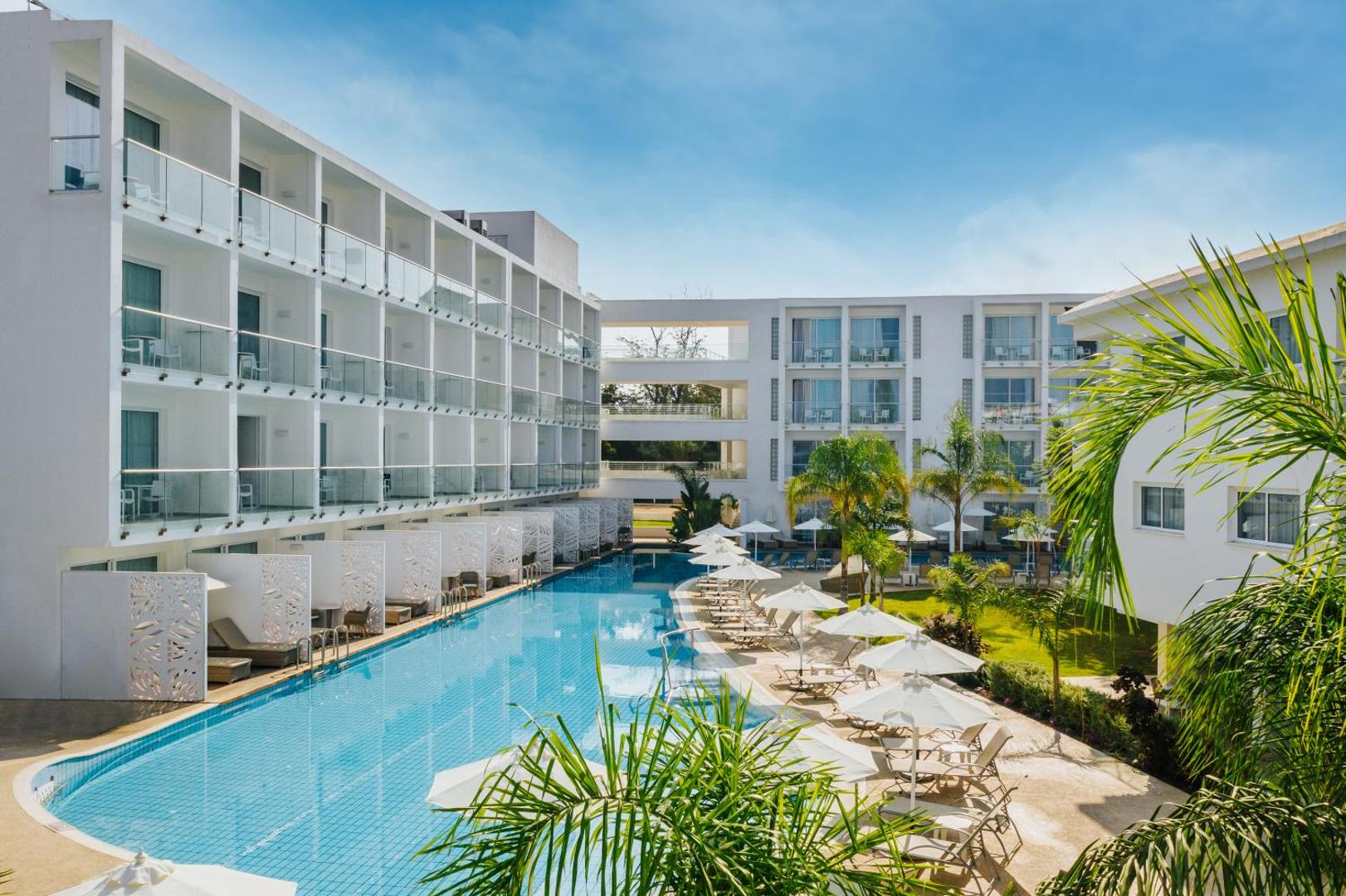 Sofianna Resort & Spa viesnīcas ēka un garais āra baseins Pafā, Kiprā — apkārtnē sauļošanās zona ar saulessargiem un palmām