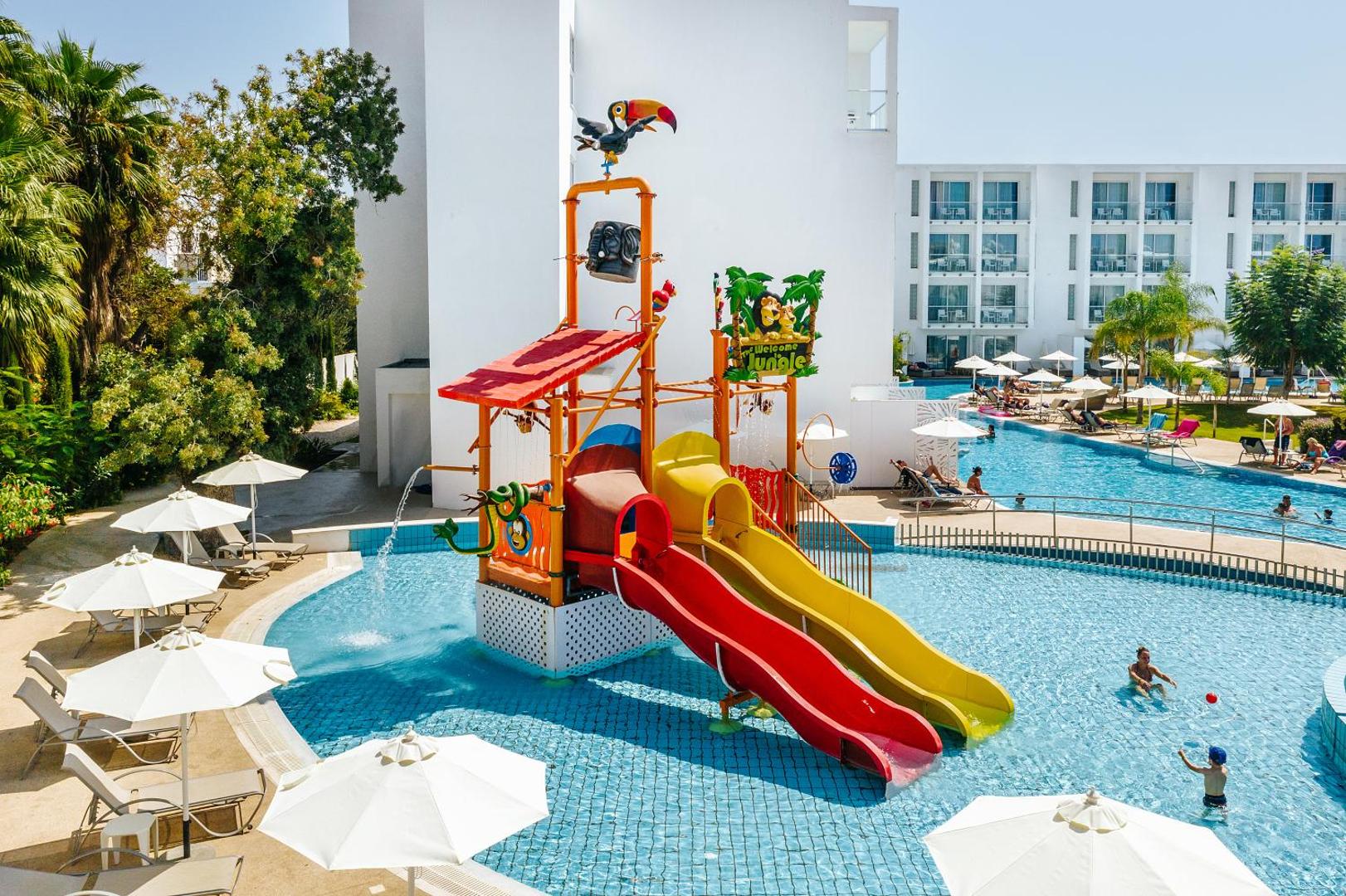 Sofianna Resort & Spa bērnu baseins ar krāsainiem slidkalniņiem un ūdens atrakcijām — plaša atpūtas zona ar saulessargiem un palmām