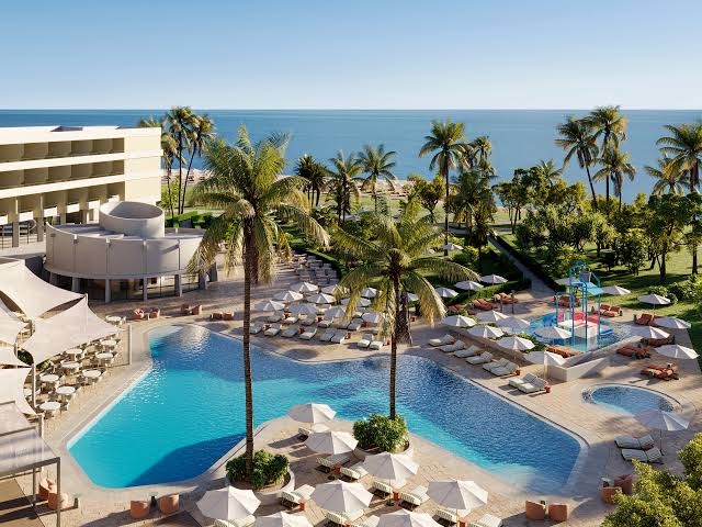 Louis Imperial Beach viesnīcas teritorija ar lielu āra baseinu, palmām un bērnu ūdens atrakcijām Pafas piekrastē, Kiprā