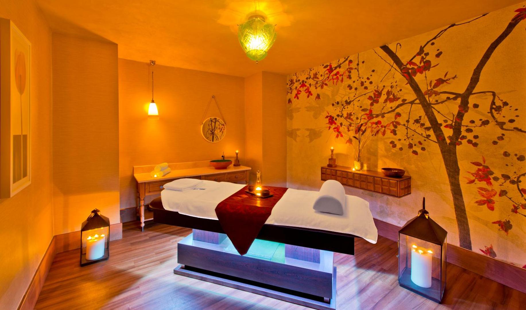 Titanic Deluxe Lara spa centra masāžas telpa ar siltu apgaismojumu, austrumnieciskiem dekoriem un profesionālu masāžas galdu