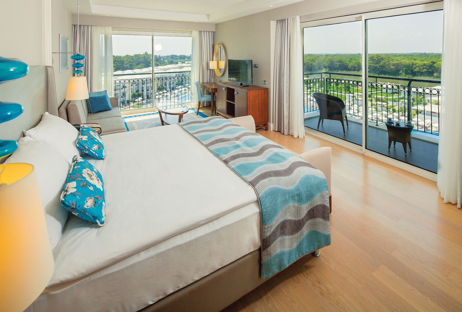 Gaišs Titanic Deluxe Golf Belek viesnīcas numurs ar balkonu, no kura paveras skats uz zaļo Belekas apkārtni un dārzu