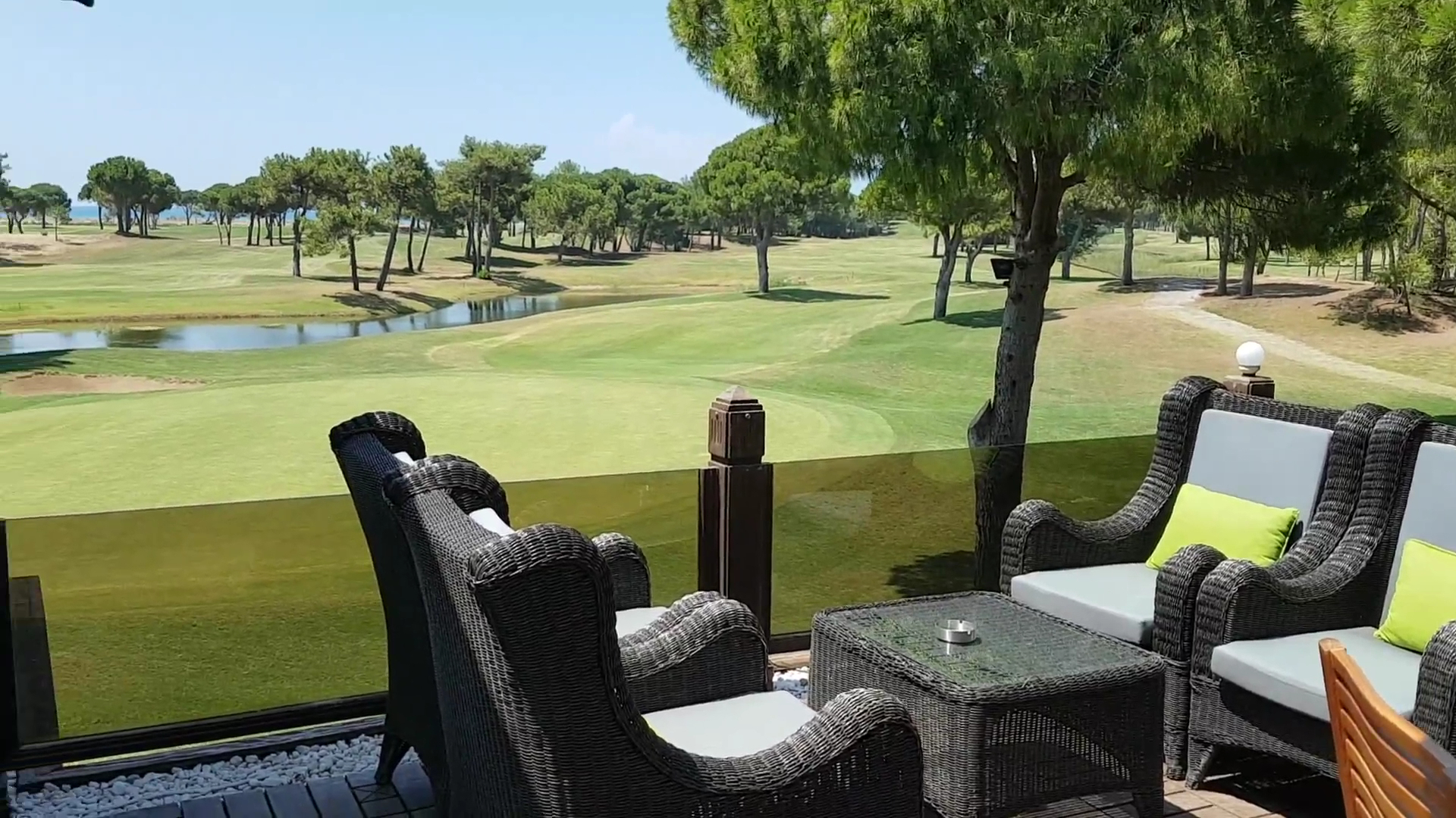 Titanic Deluxe Golf Belek terase ar pītiem atpūtas krēsliem un skatu uz plašajiem golfa laukumiem un priežu mežu Belekā