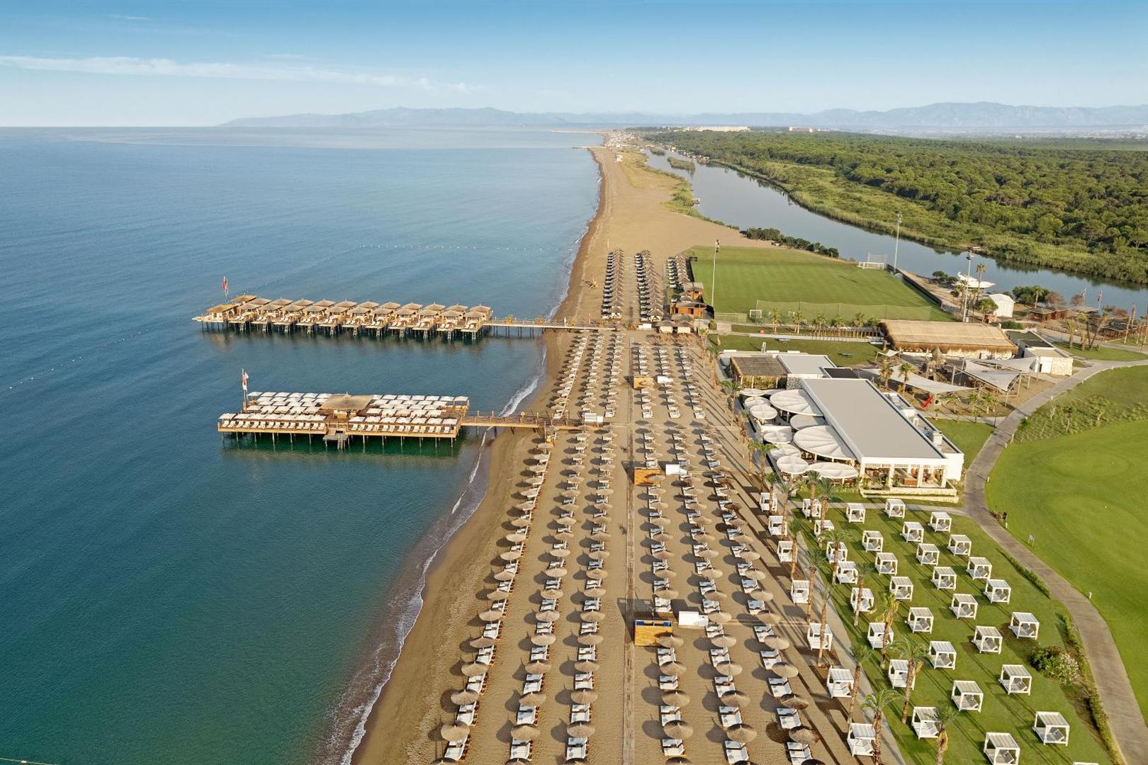 Titanic Deluxe Golf Belek plašā smilšu pludmale un kūrorta teritorija no putna lidojuma Belekā — redzama upe un jūra