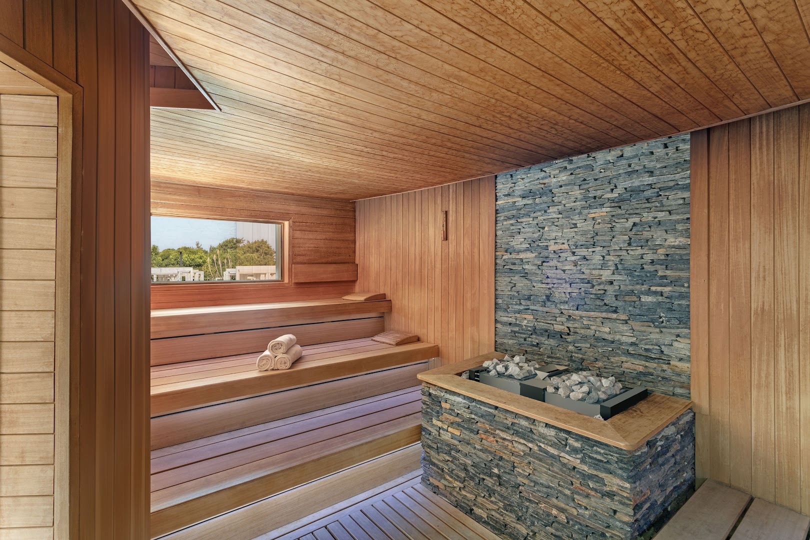 Mūsdienīga Titanic Deluxe Golf Belek sauna ar koka apdari, akmens sienas elementu un skatu caur logu uz kūrorta zaļo zonu