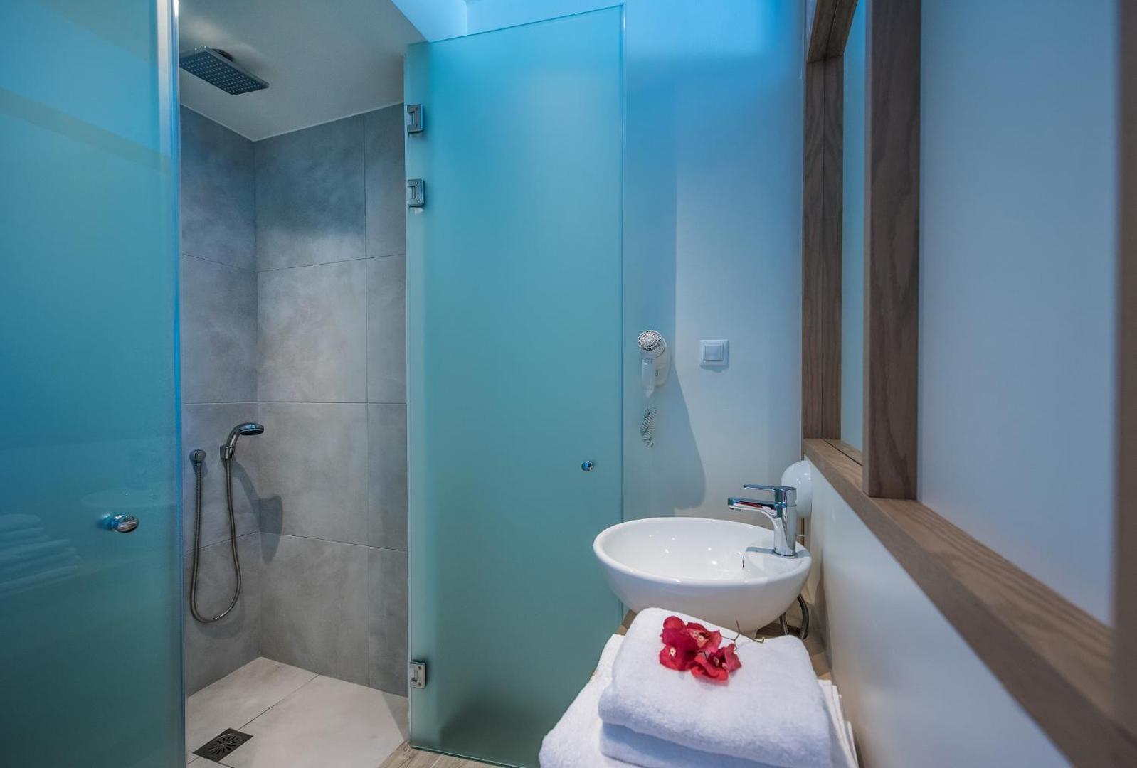 Paralos Lifestyle Beach viesnīcas numura vannas istaba Amudarā, Krētā — moderna dušas zona ar stikla durvīm, baltu izlietni un koka apdares elementiem