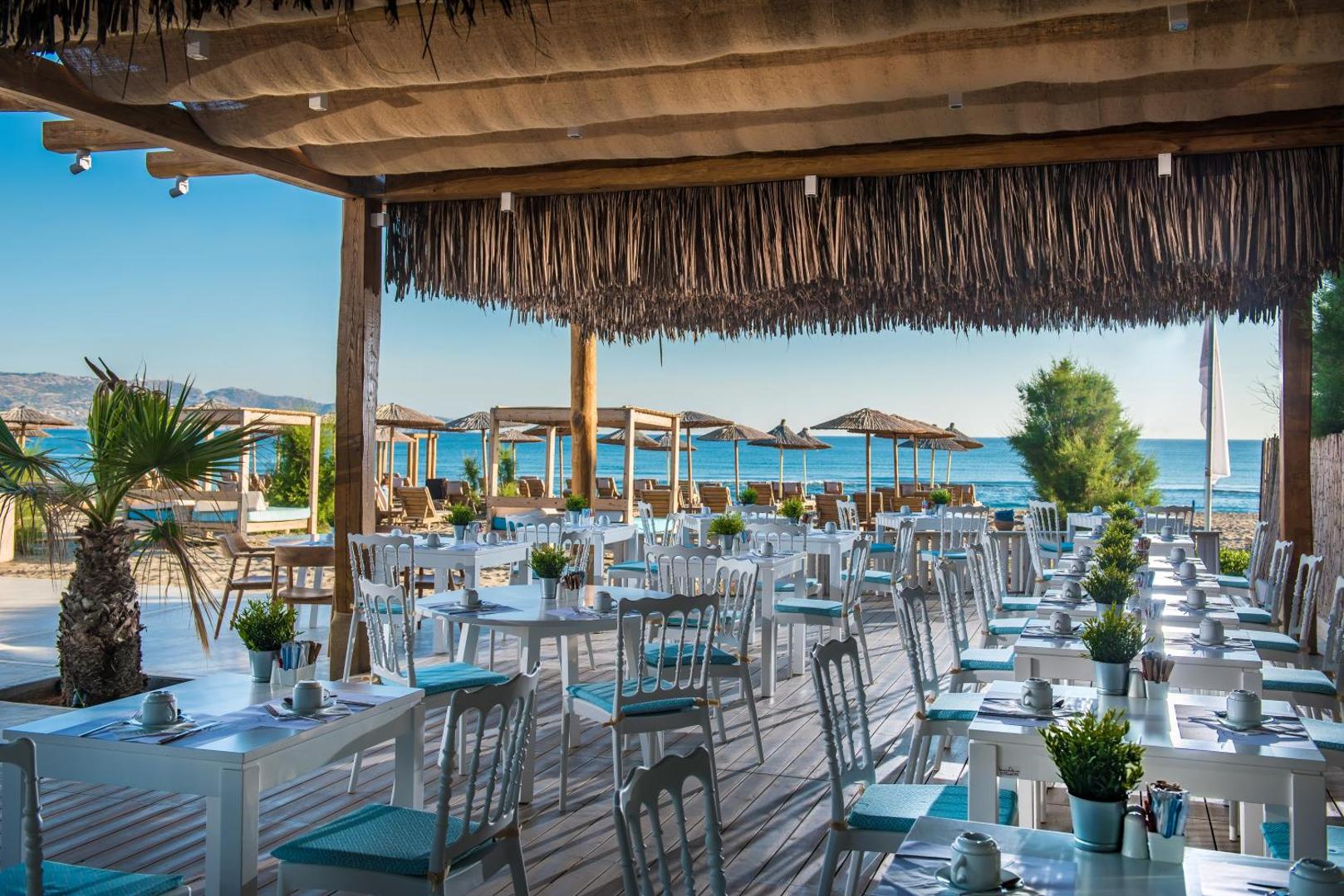 Paralos Lifestyle Beach viesnīcas āra restorāna terase ar skatu uz jūru Amudarā, Krētā — balti galdi un krēsli zem nojumes