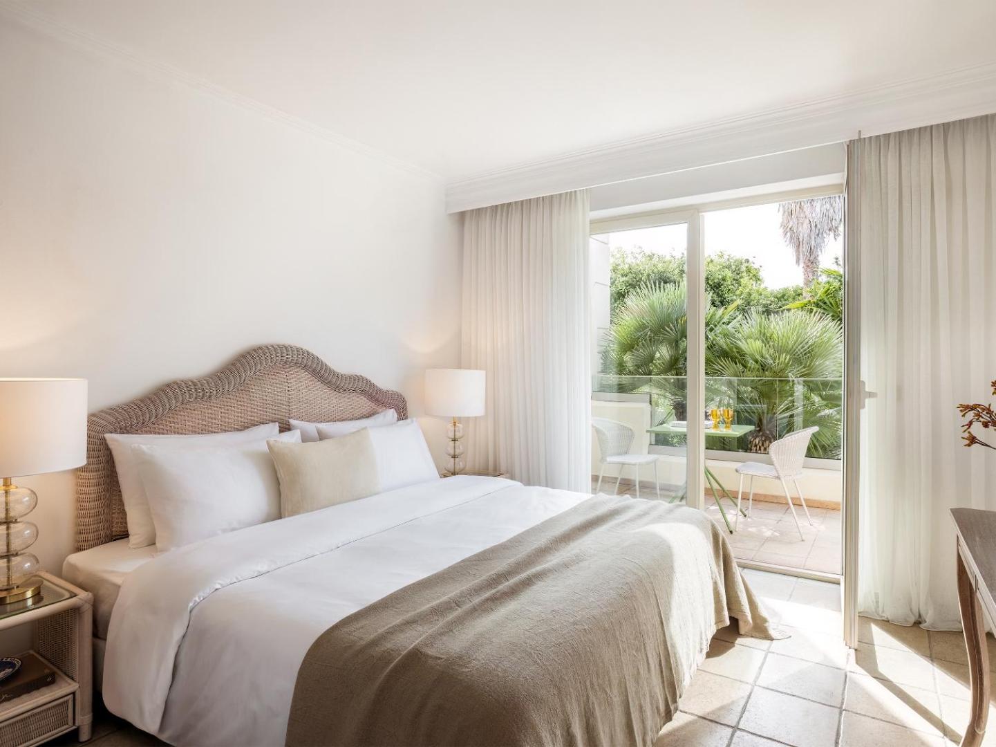 Grecotel Casa Adele plašs numurs ar divguļamo gultu un izeju uz balkonu, no kura paveras skats uz palmām