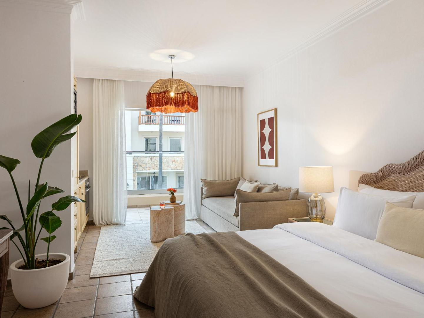 Grecotel Casa Adele viesnīcas numurs ar gaišu interjeru, dīvānu, virtuves zonu un balkonu Retimno pilsētā Krētas salā