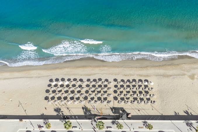 Atlantis Beach Hotel & Spa privātā pludmale Retimno no putna lidojuma — smilšu josla ar saulessargiem un dzidrs tirkīza ūdens