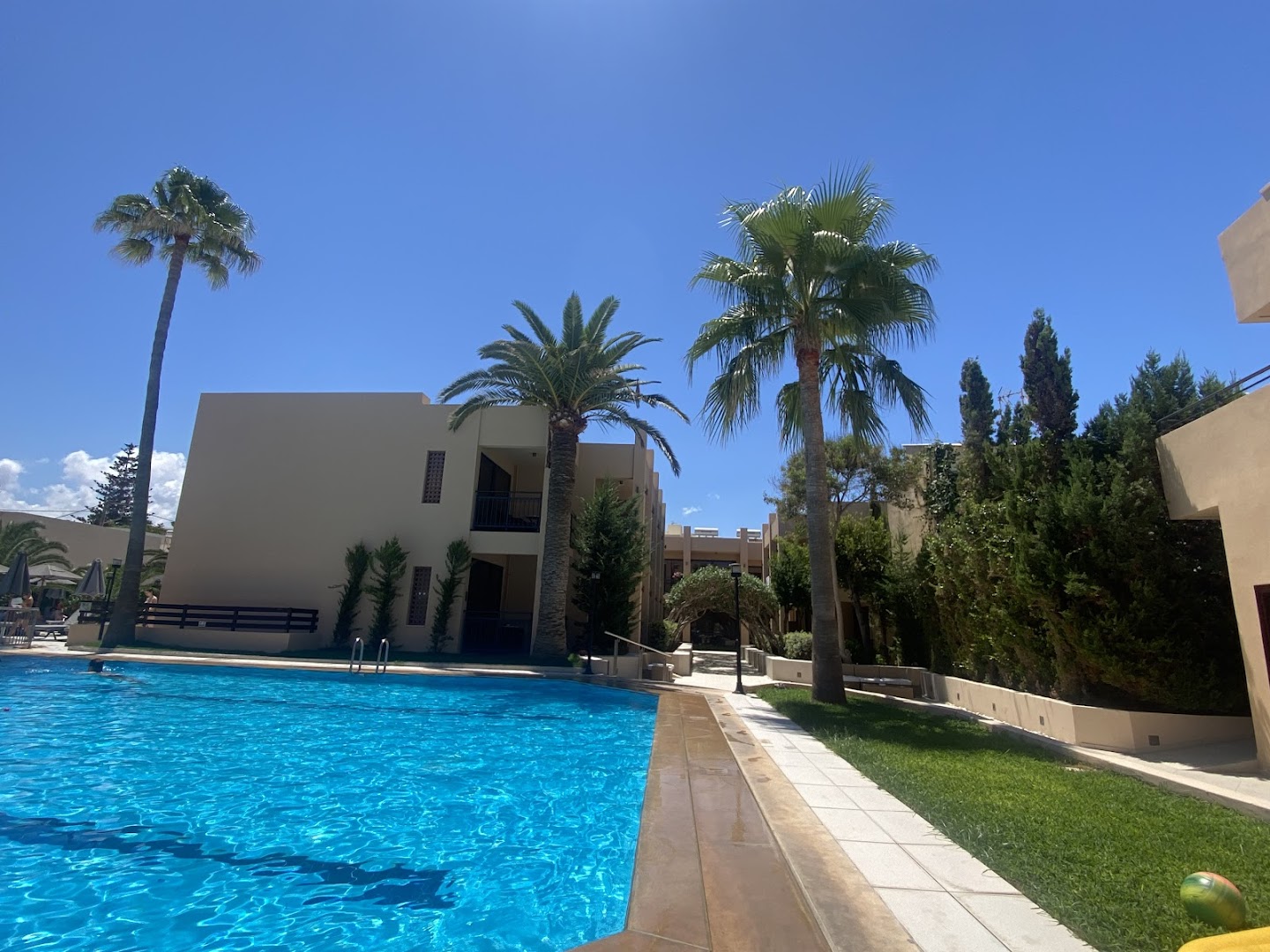 Atlantis Beach Hotel & Spa lielais āra baseins ar zilām flīzēm, palmām un viesnīcas korpusiem fonā zem skaidrām debesīm