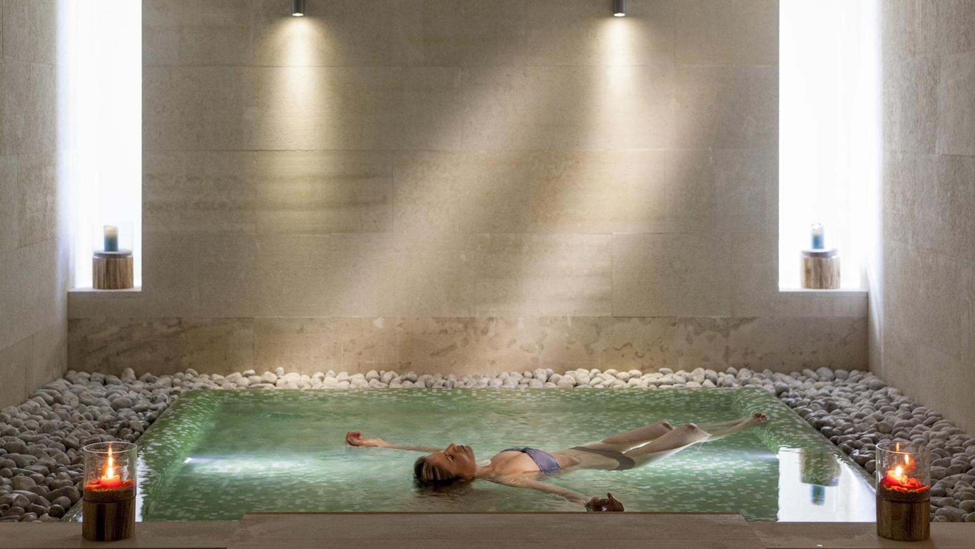Sieviete relaksējas Avra Imperial Beach Resort spa zonā, peldot siltā baseinā ar sveču gaismu un akmeņu dekorācijām
