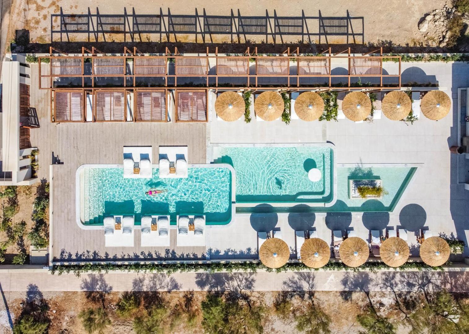 Avra Imperial Beach Resort atpūtas zona ar sauļošanās krēsliem ūdenī un salmu saulessargiem — skats no augšas