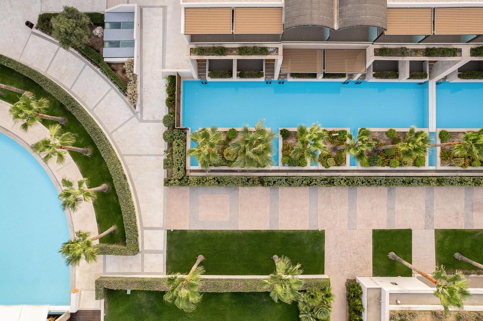 Avra Imperial Beach Resort teritorijas skats no augšas — baseini, kopti zālāji un palmas pie viesnīcas numuriem