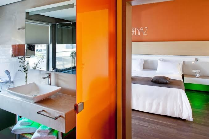 Avra Imperial Resort moderns numurs ar atvērtā plānojuma vannasistabu, oranžiem akcentiem un ērtu divguļamo gultu