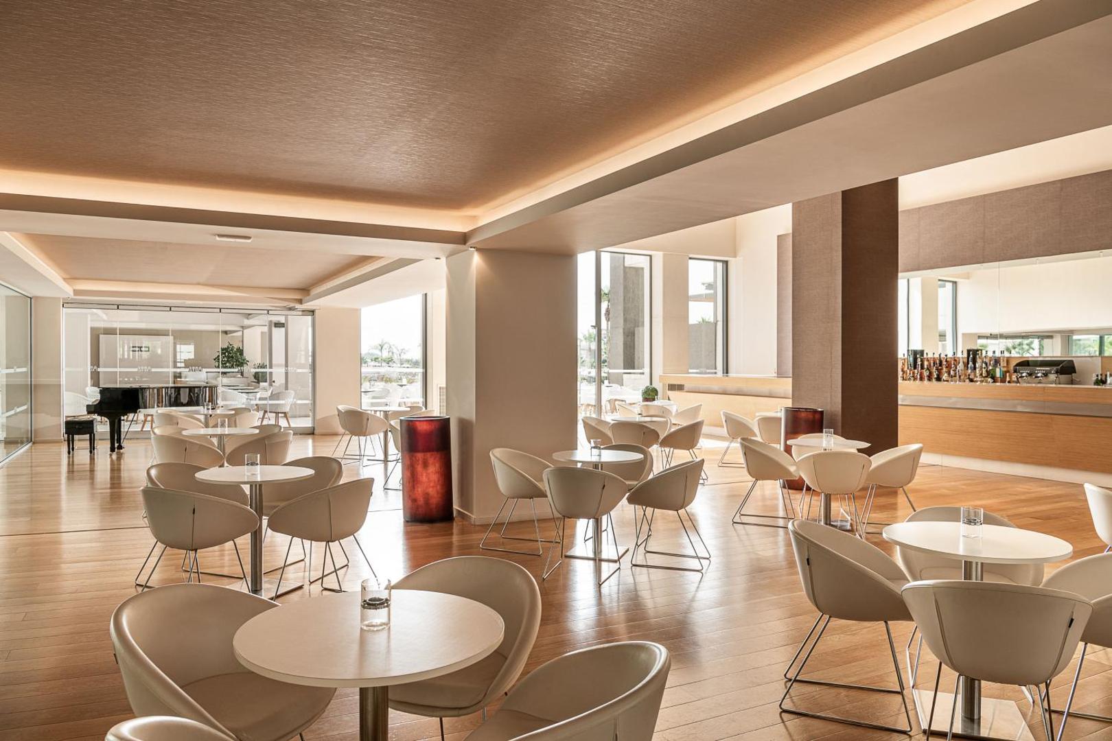 Avra Imperial Resort lobby bārs un atpūtas zona Hanijā, Krētā — gaišs interjers ar moderniem krēsliem, koka grīdu un klavierēm